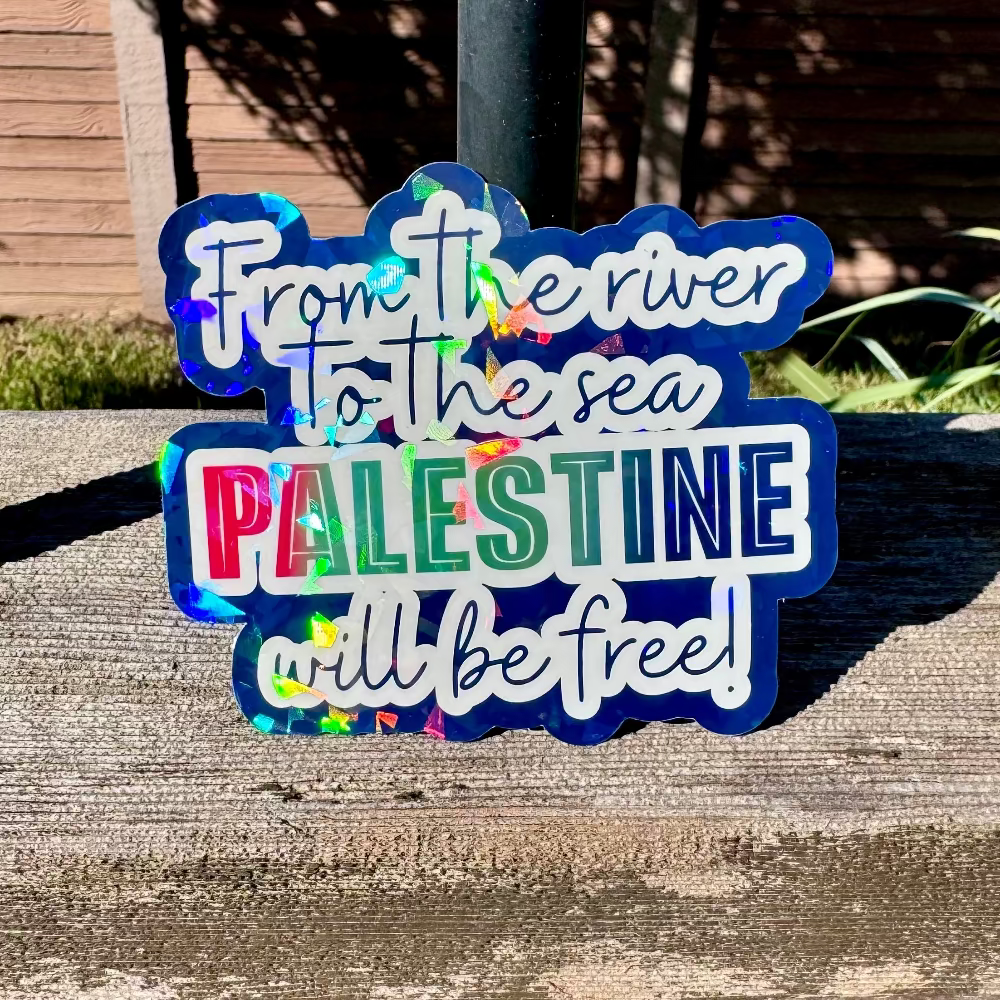 Holographic sticker with text 'From the river to the sea PALESTINE will be free!' on a wooden surface.