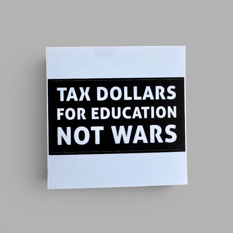 A square white sticker or sign with a black central panel and bold white text reading 'TAX DOLLARS FOR EDUCATION NOT WARS', shown on a plain light gray background.