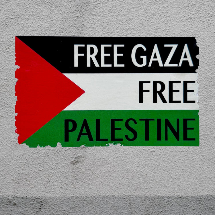 A rectangular Palestine flag sticker with the words 'FREE GAZA', 'FREE', and 'PALESTINE' in bold black letters, applied to a textured light gray wall.